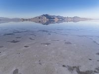 this photo was taken from an airplane window of a barren land, with small clouds and mountains reflecting in the water