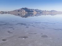 this photo was taken from an airplane window of a barren land, with small clouds and mountains reflecting in the water