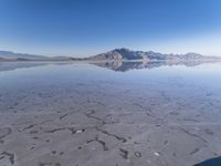 this photo was taken from an airplane window of a barren land, with small clouds and mountains reflecting in the water