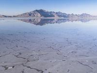 this photo was taken from an airplane window of a barren land, with small clouds and mountains reflecting in the water