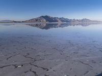 this photo was taken from an airplane window of a barren land, with small clouds and mountains reflecting in the water