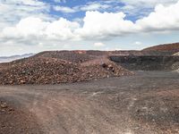 dirt covered hillside with rocks and small piles under blue cloudy skies in a barren landscape