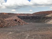 dirt covered hillside with rocks and small piles under blue cloudy skies in a barren landscape