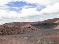 dirt covered hillside with rocks and small piles under blue cloudy skies in a barren landscape