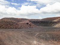 dirt covered hillside with rocks and small piles under blue cloudy skies in a barren landscape