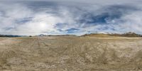 a wide angle shot of a barren dirt field in the distance, with a few clouds in the sky