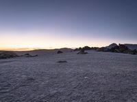 an empty field is covered in snow and rocks at sunset over the mountainside, which are very barren