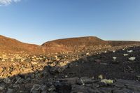 the barren landscape of the mountains of rocky terrain is surrounded by boulders and vegetation against the backdrop of a blue sky with clouds