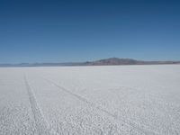 a barren plain with tire tracks in the middle of it is surrounded by mountains and a clear blue sky