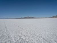 a barren plain with tire tracks in the middle of it is surrounded by mountains and a clear blue sky