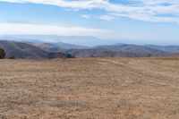 a man stands in a barren valley in the distance are mountains and trees in the distance