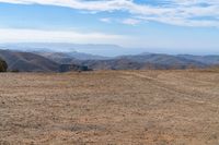 a man stands in a barren valley in the distance are mountains and trees in the distance