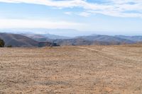 a man stands in a barren valley in the distance are mountains and trees in the distance