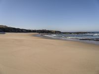 the sandy beach with waves rolling towards the shoreline near a house by the water, with waves breaking into the shore