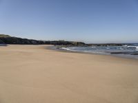 the sandy beach with waves rolling towards the shoreline near a house by the water, with waves breaking into the shore