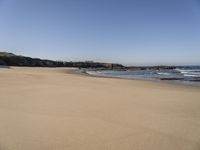 the sandy beach with waves rolling towards the shoreline near a house by the water, with waves breaking into the shore