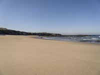 the sandy beach with waves rolling towards the shoreline near a house by the water, with waves breaking into the shore