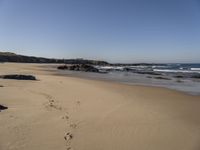 a sandy beach next to the ocean with footprints on the sand and water coming in