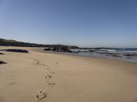 a sandy beach next to the ocean with footprints on the sand and water coming in