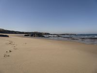 a sandy beach next to the ocean with footprints on the sand and water coming in