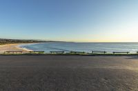 a street view of a beach and two benches by the ocean with clear skies above