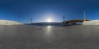 an empty beach with a bridge near the water and sand dunes, with the sun shining through