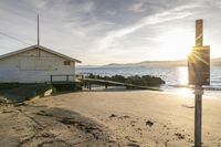 the house sits on the beach behind a rope in the sand at sunset with boats in the water