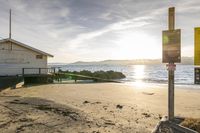 the house sits on the beach behind a rope in the sand at sunset with boats in the water