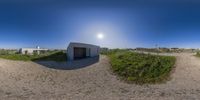 a panoramic image of an outside house made from sand on the beach with bright sun