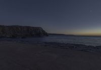 the moon rises over the water and rocks in the foreground as the sky approaches