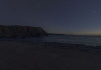 the moon rises over the water and rocks in the foreground as the sky approaches