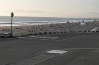 an empty road near a beach and waves as well as cars on the sand and houses on the beach