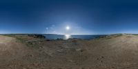 a view of the sun from a dirt hill on the beach with two people on the horizon