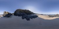 several rocks on a beach near water with large boulders on top of them and a clear blue sky above