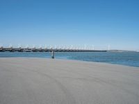 a pier with windmill in the background and the ocean visible from its sand area nearby