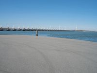 a pier with windmill in the background and the ocean visible from its sand area nearby