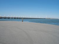 a pier with windmill in the background and the ocean visible from its sand area nearby