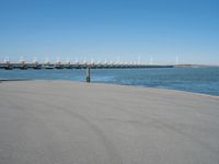 a pier with windmill in the background and the ocean visible from its sand area nearby