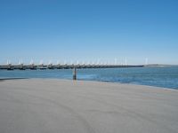 a pier with windmill in the background and the ocean visible from its sand area nearby