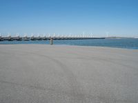 a pier with windmill in the background and the ocean visible from its sand area nearby