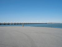 a pier with windmill in the background and the ocean visible from its sand area nearby