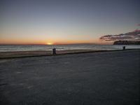 two people are sitting on an empty bench in front of the ocean at sunset with a dog in the foreground