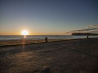 two people are sitting on an empty bench in front of the ocean at sunset with a dog in the foreground