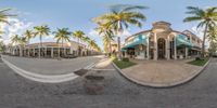 a 360 - lens image of a small building in the middle of palm trees lined streets