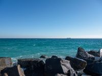 a view of the sea and a ship in the distance at the beach, with large rocks and turquoise water