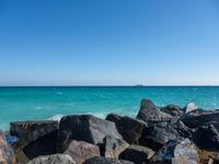 a view of the sea and a ship in the distance at the beach, with large rocks and turquoise water