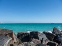 a view of the sea and a ship in the distance at the beach, with large rocks and turquoise water
