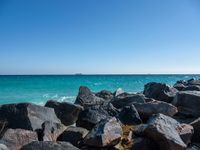 a view of the sea and a ship in the distance at the beach, with large rocks and turquoise water