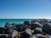 a view of the sea and a ship in the distance at the beach, with large rocks and turquoise water