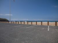 an empty parking lot on the beach next to the ocean by some tall poles and poles